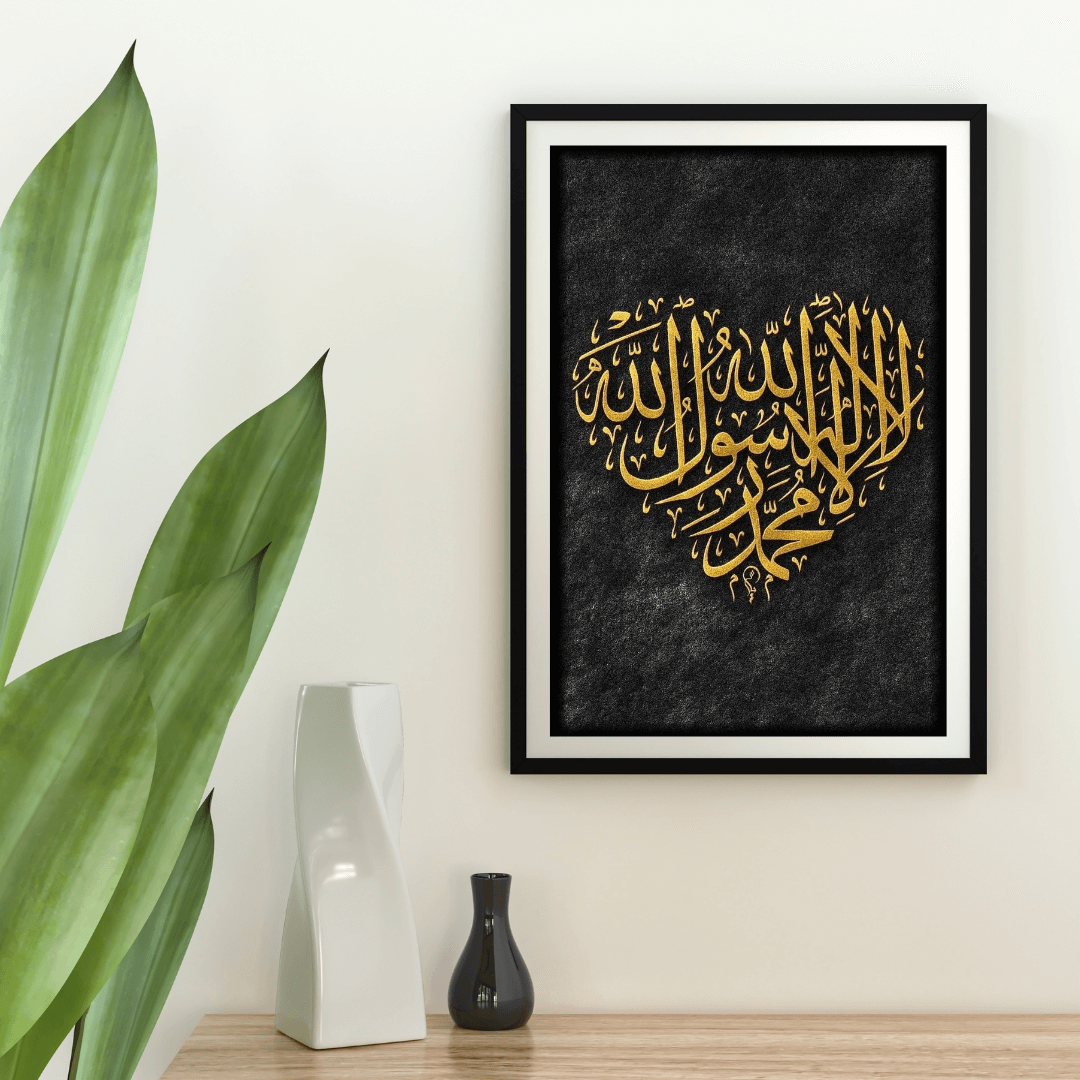 Framed artwork with gold calligraphy on a black background, placed on a wooden surface with decorative vases and a plant.