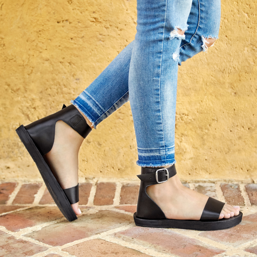 Person wearing black sandals with a yellow wall and brick floor background