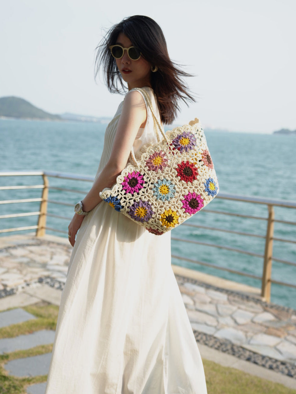 Woman holding a colorful floral-patterned bag by the sea