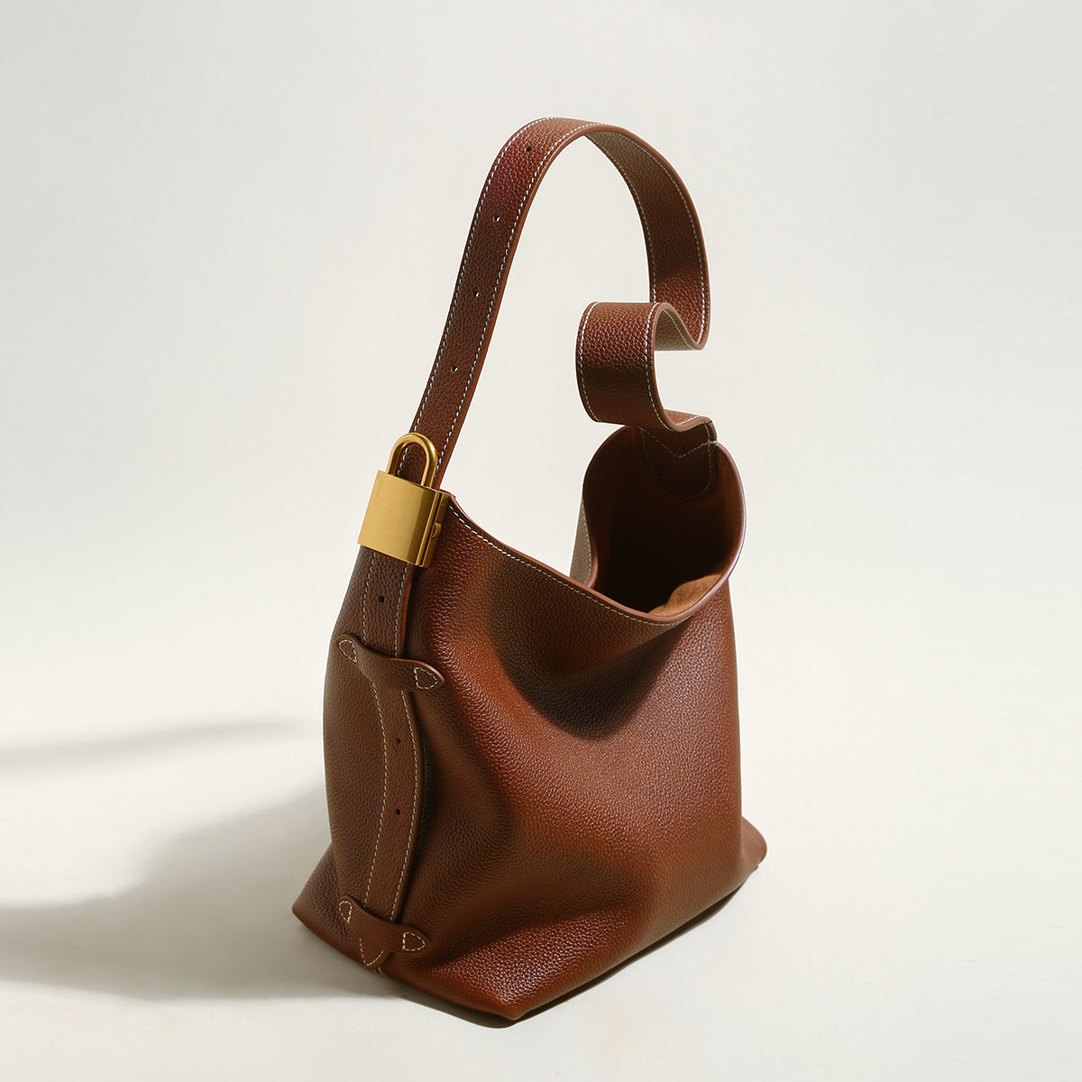 Brown leather handbag with a gold buckle on a light background