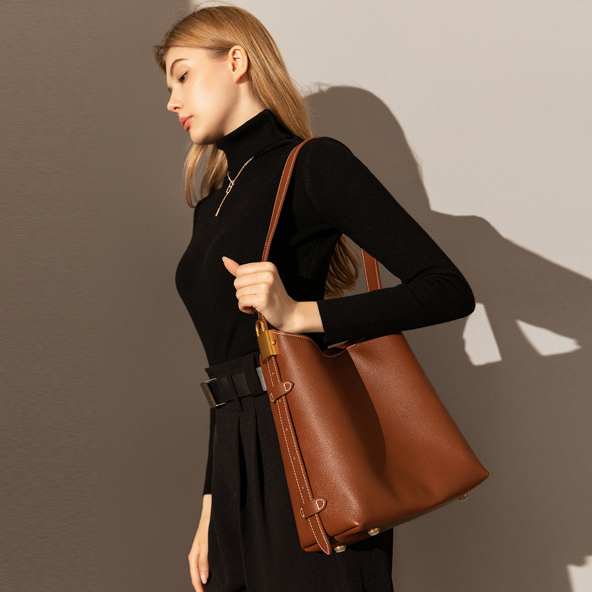 Woman holding a brown leather handbag against a plain background