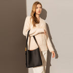 Woman holding a black handbag against a gradient wall