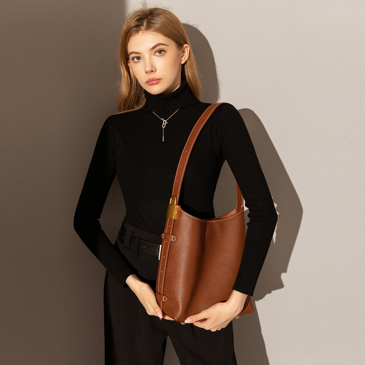 Woman holding a brown leather bag against a neutral background