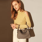 Woman in a yellow sweater holding a Monte Convertible Shoulder Bag, showcasing its elegant design and gold-plated hardware.