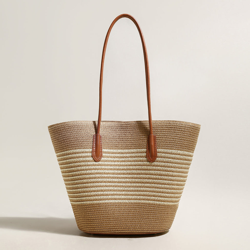 Woven straw tote bag with brown leather handles on a light beige background