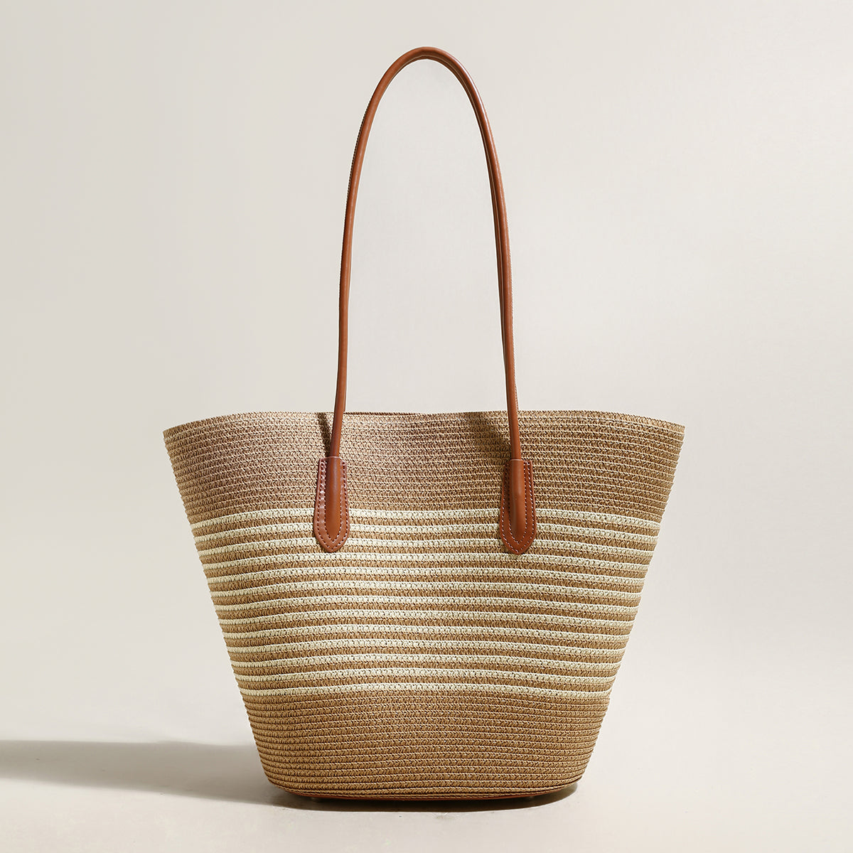 Woven straw tote bag with brown leather handles on a light beige background