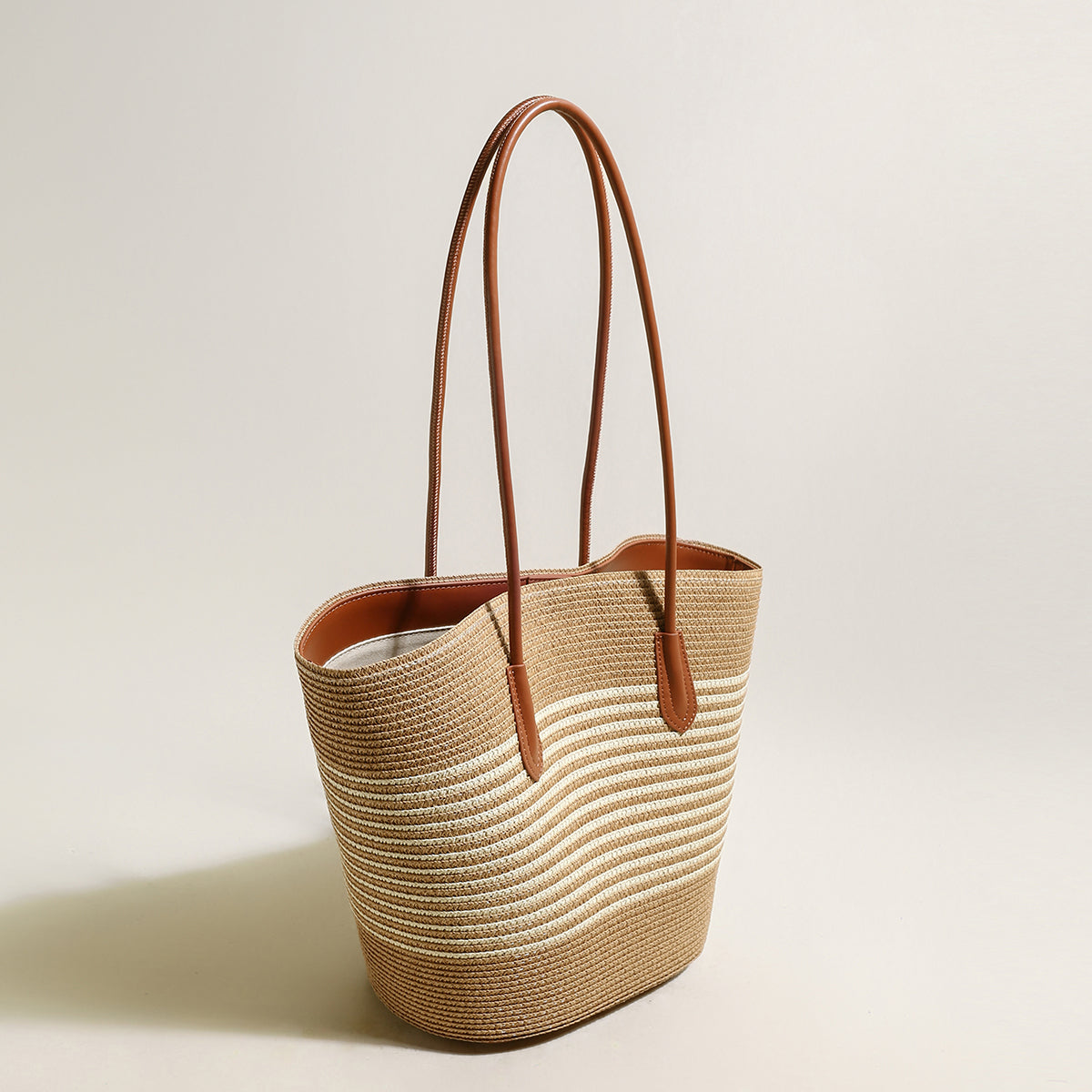 Woven straw tote bag with brown leather handles on a light beige background