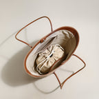 Brown baby bassinet with a beige drawstring bag inside on a light background