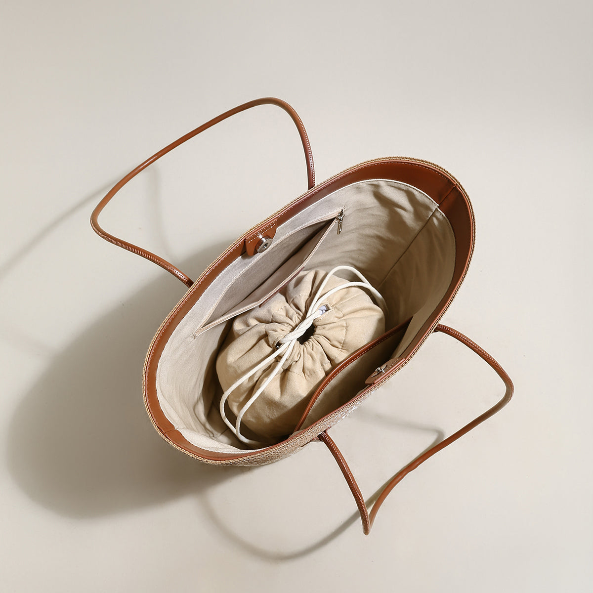 Brown baby bassinet with a beige drawstring bag inside on a light background