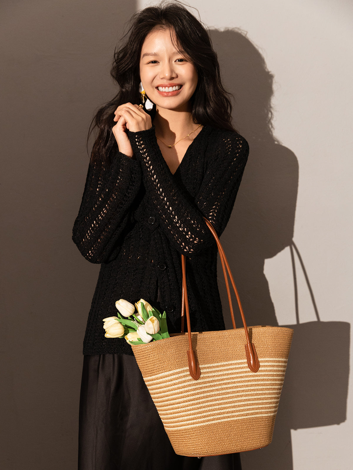 Woman holding a straw bag with flowers against a plain background