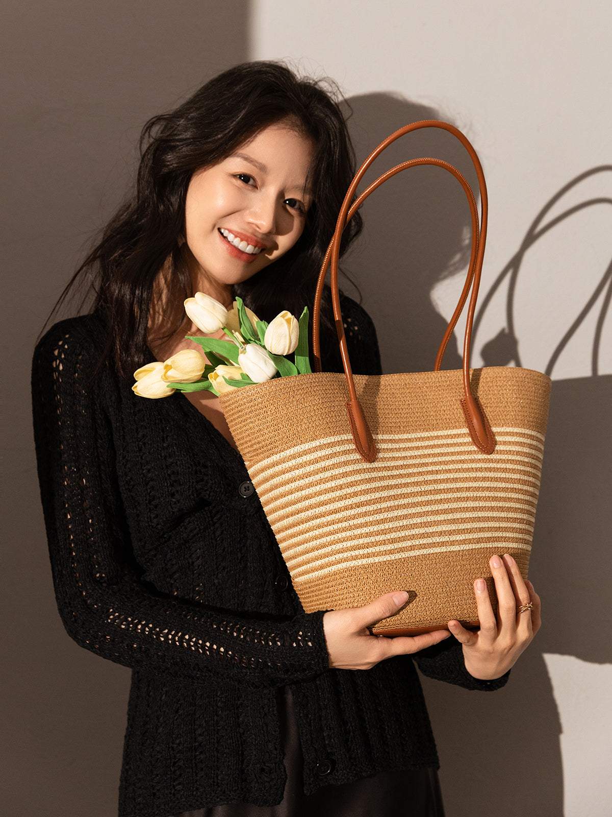 Woman holding a woven handbag with flowers against a plain background