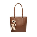 Brown tote bag with a teddy bear charm on a white background