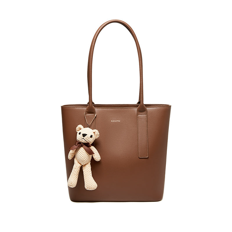Brown tote bag with a teddy bear charm on a white background