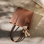 Brown leather handbag with a teddy bear attached on a textured surface