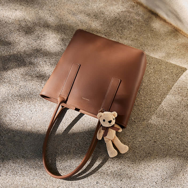 Brown leather handbag with a teddy bear attached on a textured surface