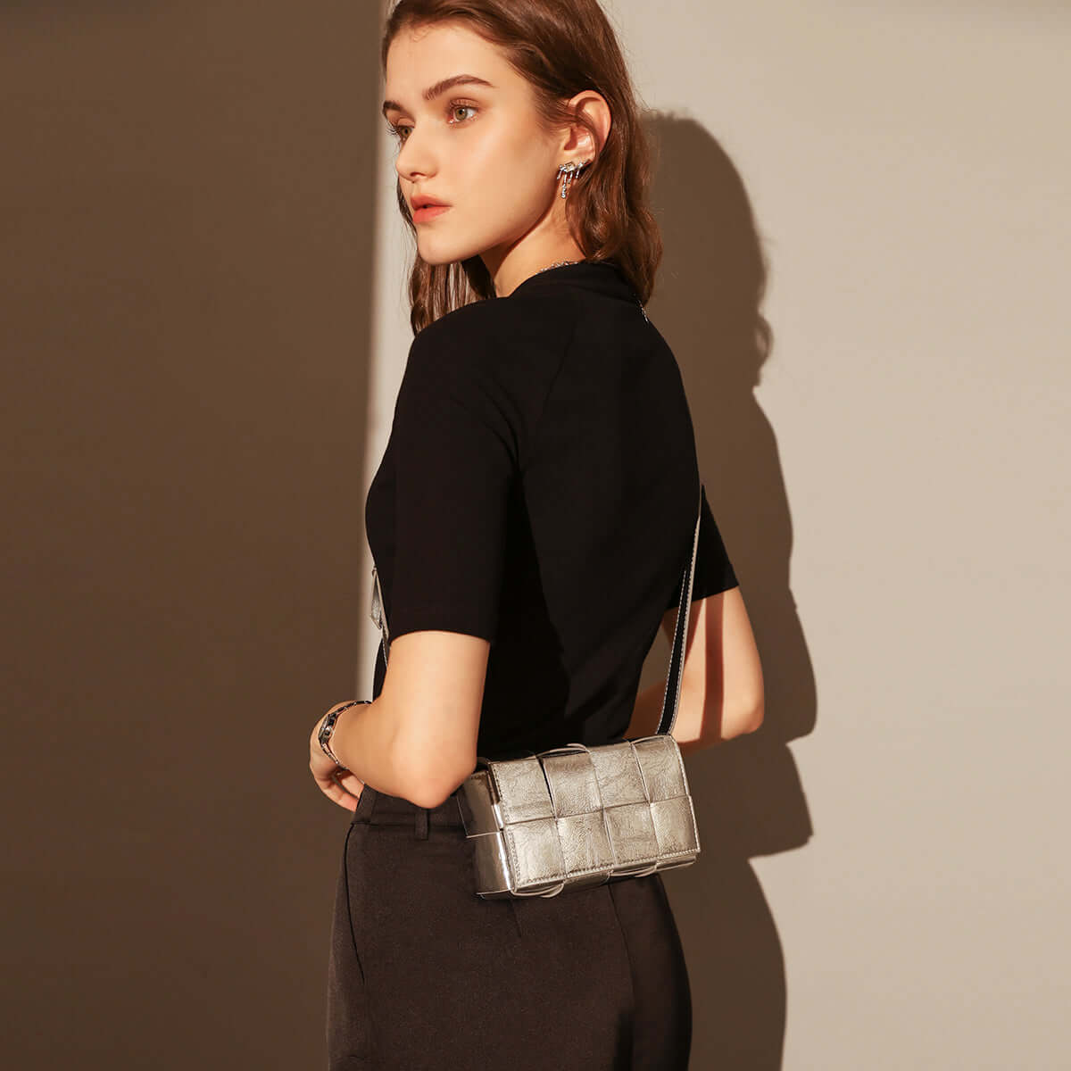 Woman holding a silver handbag against a neutral background